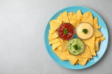 Photo of Blue plate with tasty Mexican nachos chips and sauces on grey table, top view. Space for text