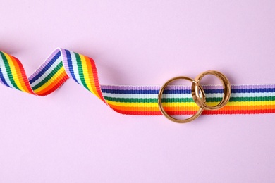 Wedding rings and rainbow ribbon on color background, top view. Gay symbol