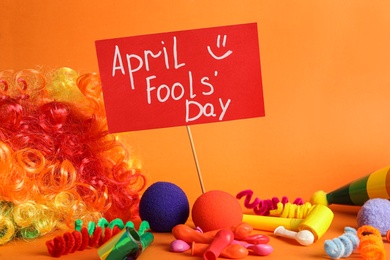 Photo of Sign with phrase Happy Fools' Day and clown's accessories on orange background