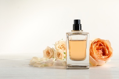 Elegant bottle of perfume and flowers on light background, space for text