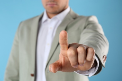 Photo of Businessman pointing at something on light blue background, closeup. Finger gesture