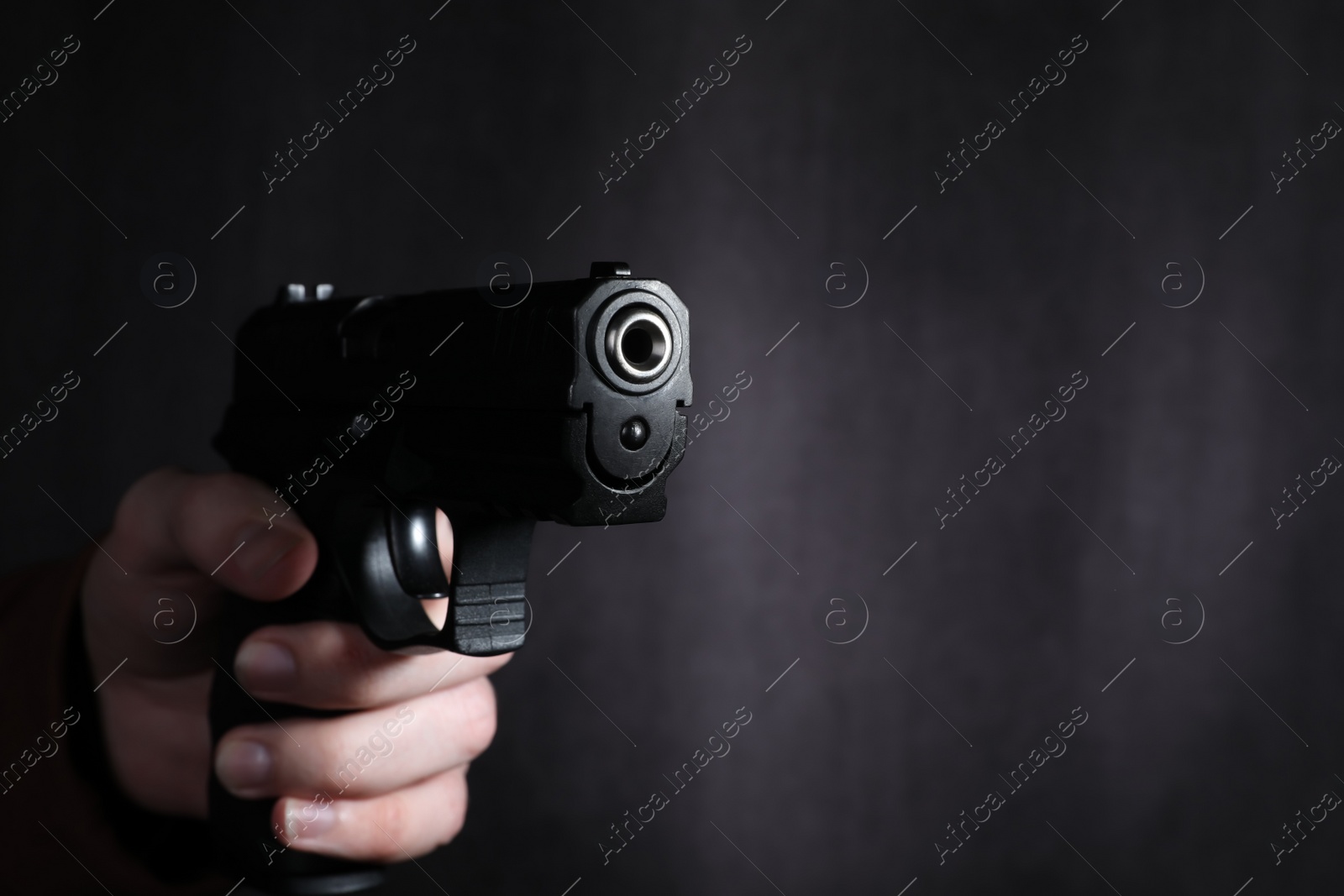 Photo of Man aiming gun against dark background, closeup. Space for text