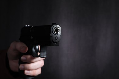 Photo of Man aiming gun against dark background, closeup. Space for text