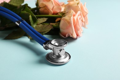 Photo of Stethoscope and flowers on light blue background, closeup with space for text. Happy Doctor's Day