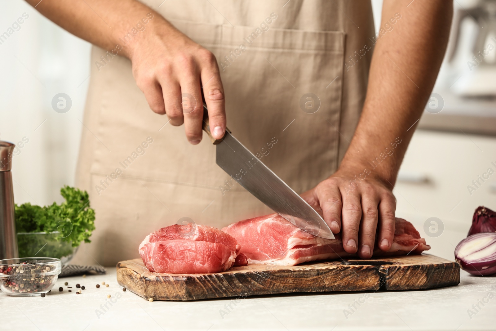 Photo of Man cutting fresh raw meat on table in kitchen, closeup