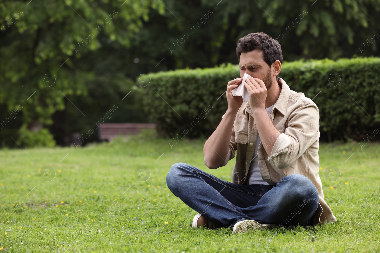 Photo of Man suffering from seasonal spring allergy on green grass in park. Space for text