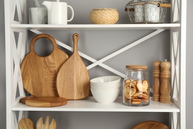 Photo of Wooden cutting boards, dishware, kitchen utensils and french palmier cookies on shelving unit