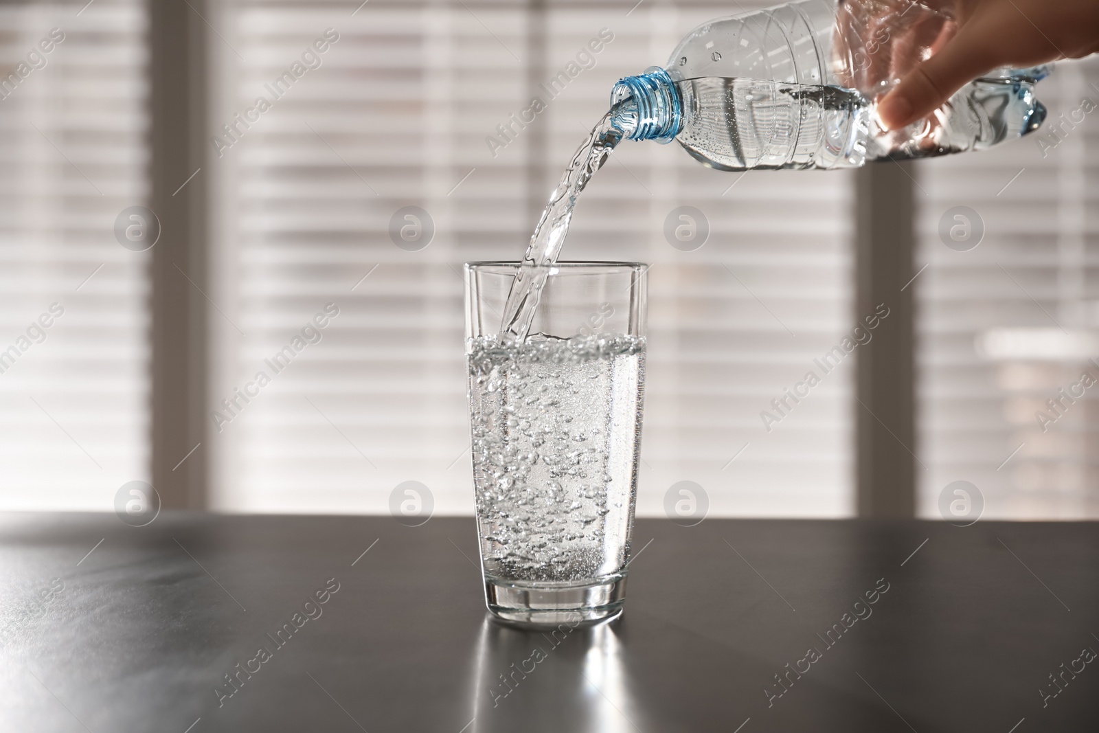 Photo of Person pouring water from bottle into glass on table against blurred background, closeup