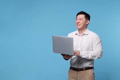 Photo of Happy man with laptop on light blue background, space for text