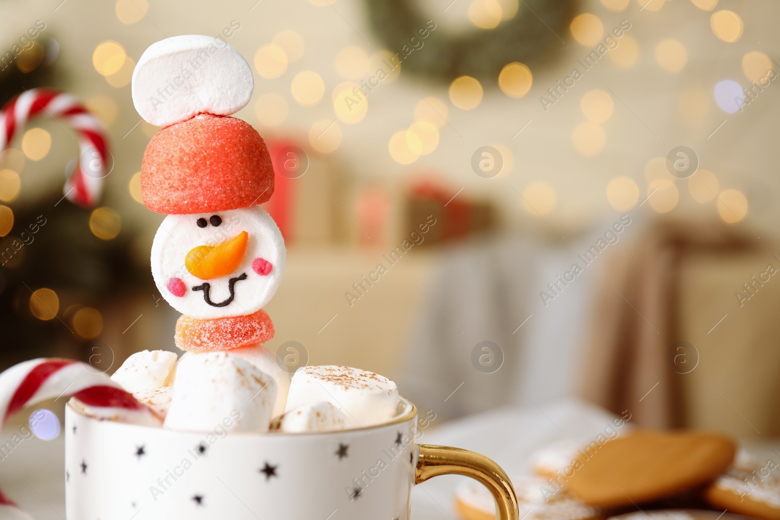 Photo of Funny marshmallow snowman in cup of hot drink against blurred festive lights, closeup. Space for text