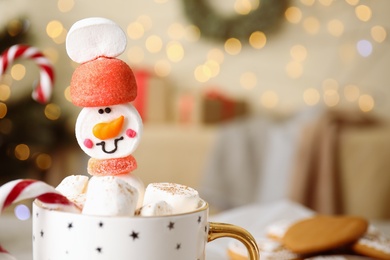 Photo of Funny marshmallow snowman in cup of hot drink against blurred festive lights, closeup. Space for text