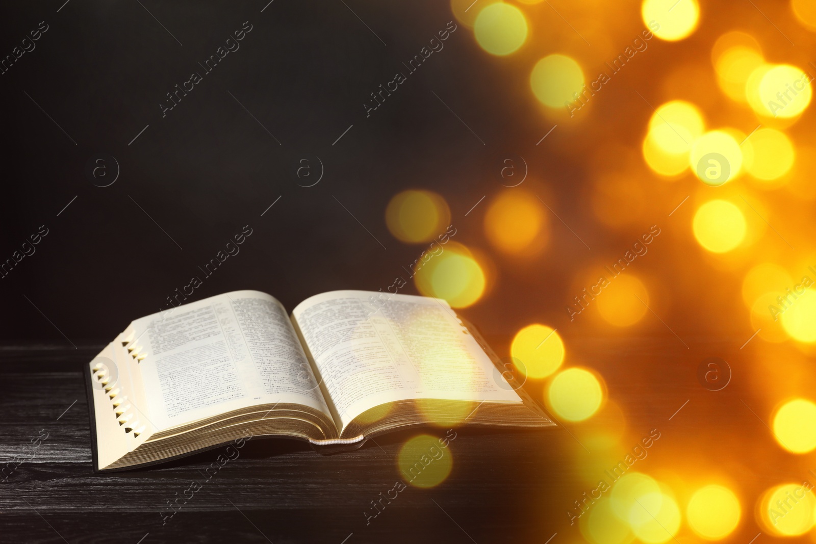 Image of Open Bible on black wooden table, bokeh effect