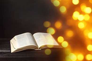 Image of Open Bible on black wooden table, bokeh effect