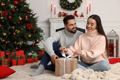 Photo of Happy young woman opening gift from her boyfriend in room decorated for Christmas