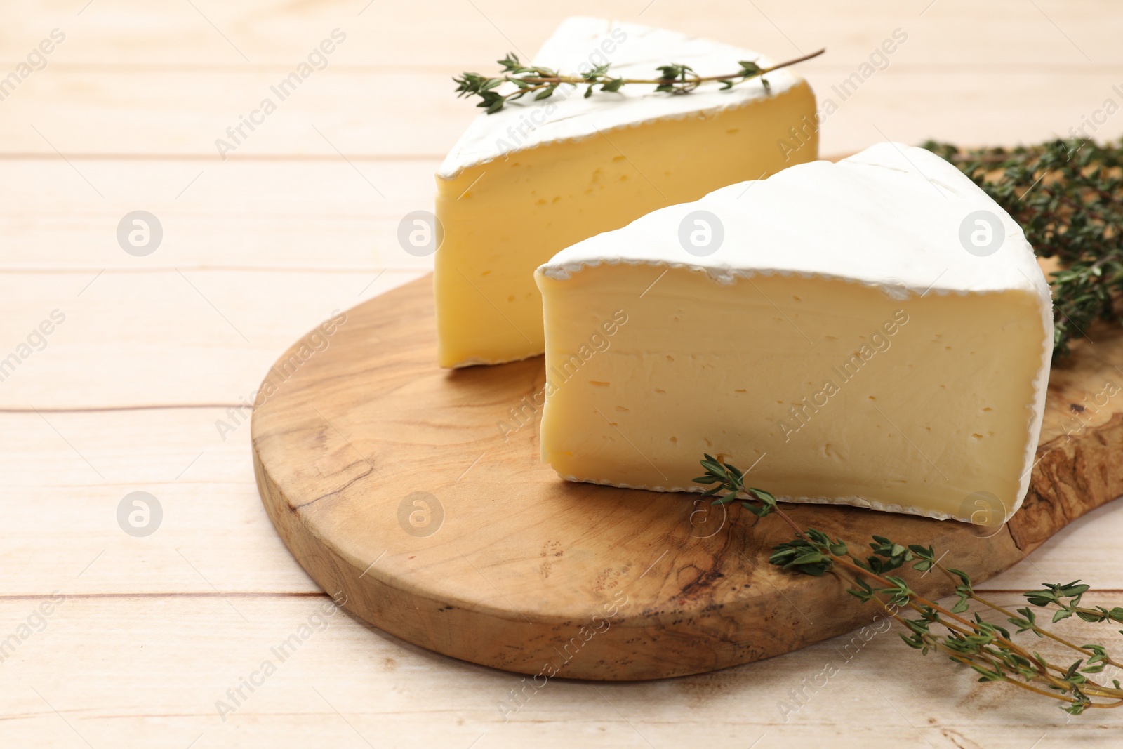 Photo of Board with pieces of tasty camembert cheese and thyme on light wooden table, closeup. Space for text