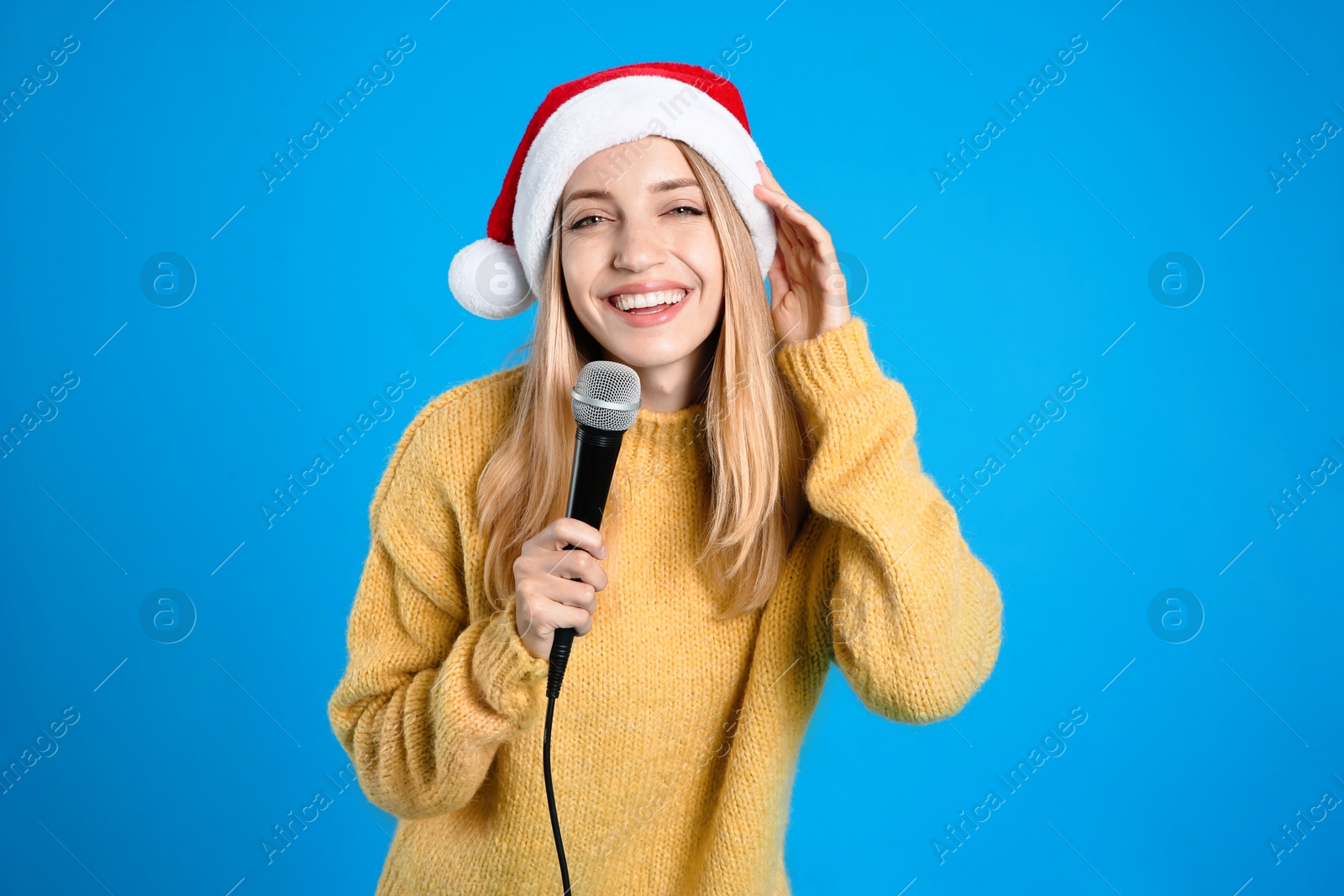 Photo of Happy woman in Santa Claus hat singing with microphone on blue background. Christmas music