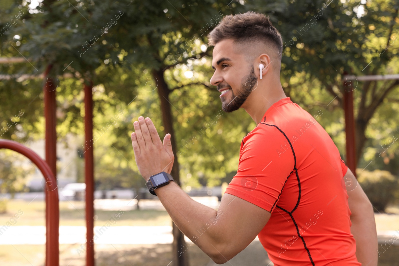 Photo of Young man with wireless headphones listening to music while exercising on sports ground. Space for text