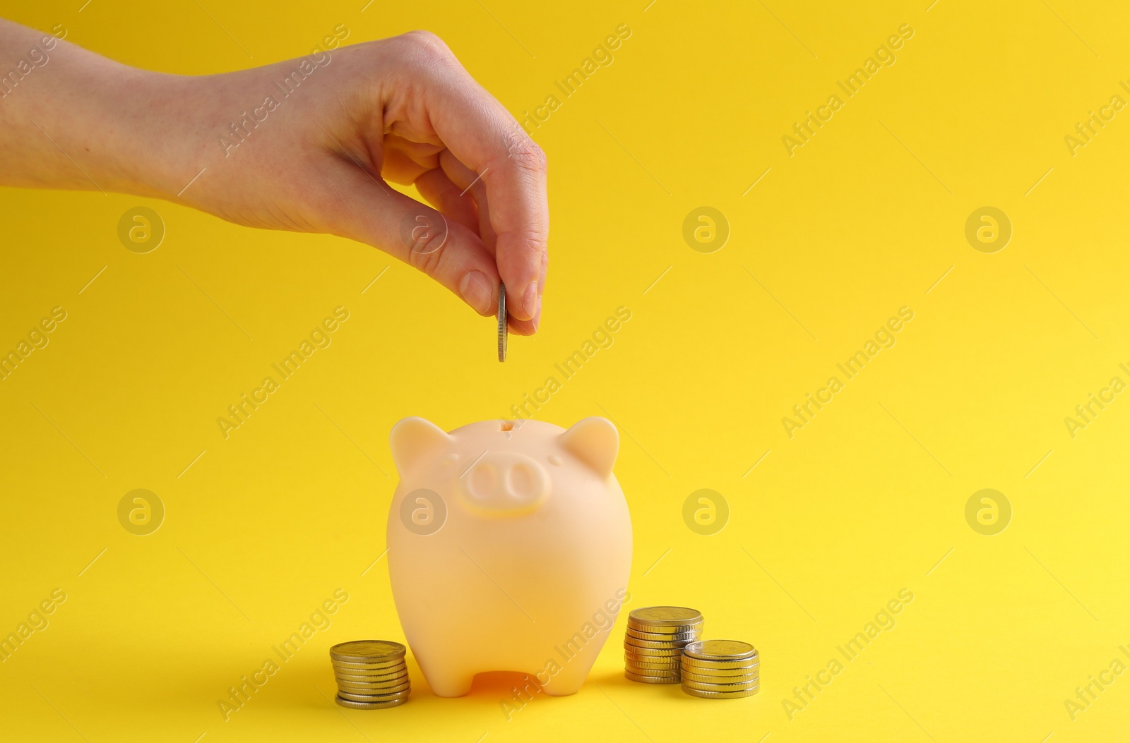 Photo of Financial savings. Woman putting coin into piggy bank on yellow background, closeup