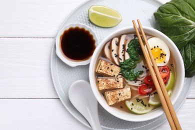 Photo of Delicious vegetarian ramen, soy sauce and pak choy leaves on white wooden table, top view. Space for text
