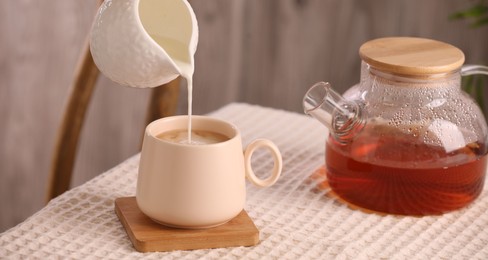 Photo of Pouring milk into cup with aromatic tea at table