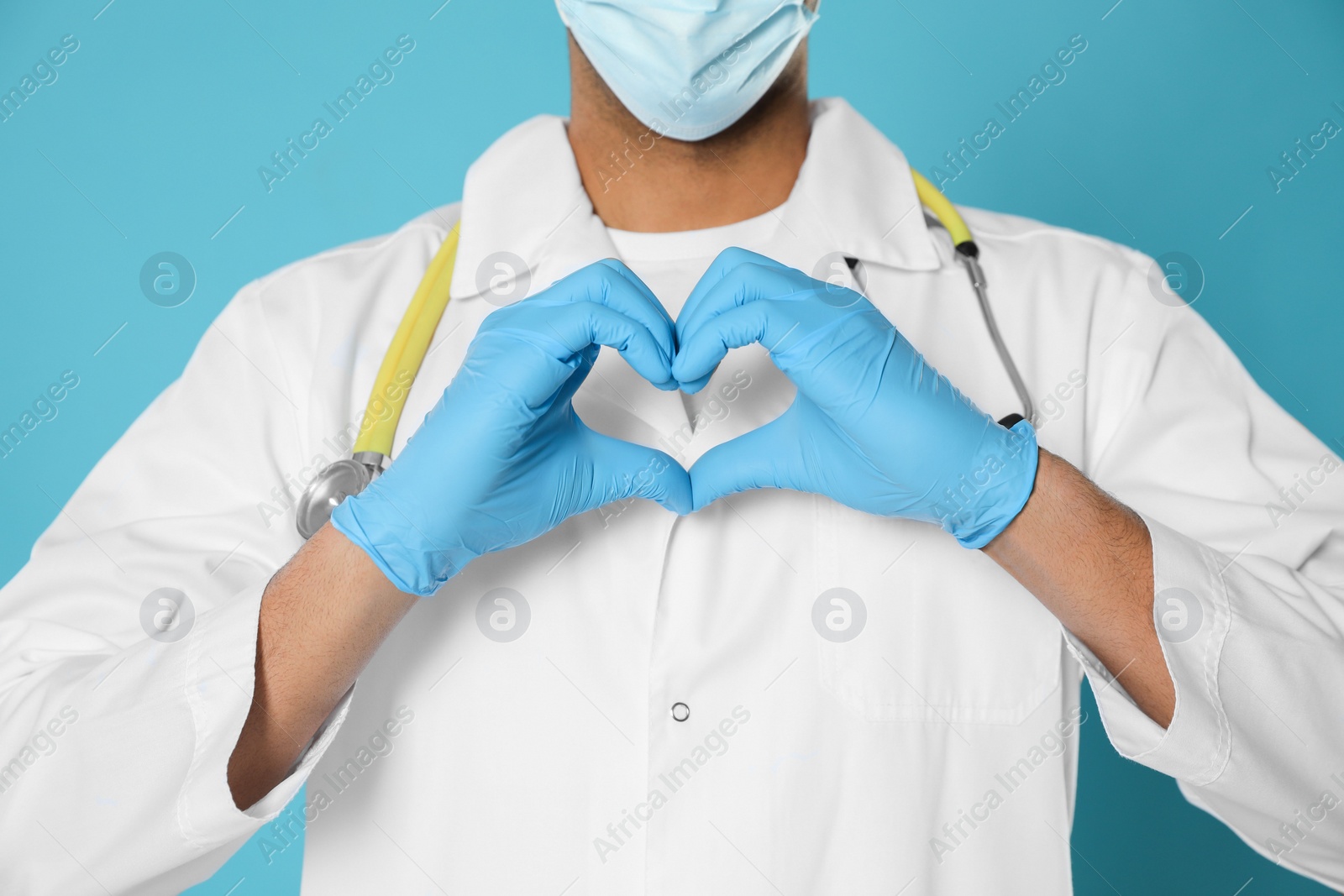 Photo of Doctor or medical assistant (male nurse) in uniform making heart with hands turquoise background, closeup