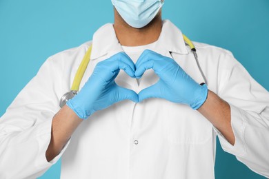 Doctor or medical assistant (male nurse) in uniform making heart with hands turquoise background, closeup