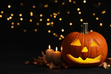 Photo of Pumpkin jack o'lantern, candles and autumn leaves  on table against blurred background, space for text. Halloween decor