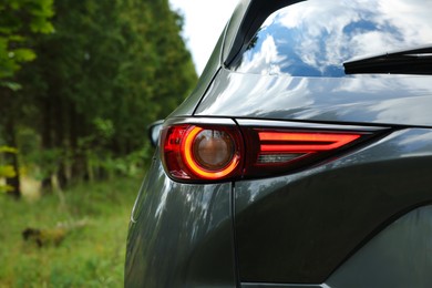 Photo of New black modern car on road near trees, closeup of taillight