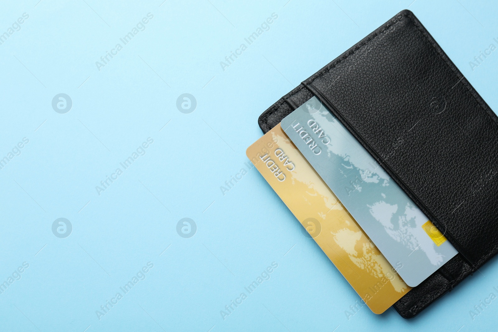 Photo of Leather card holder with credit cards on light blue background, top view. Space for text