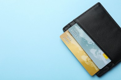 Leather card holder with credit cards on light blue background, top view. Space for text