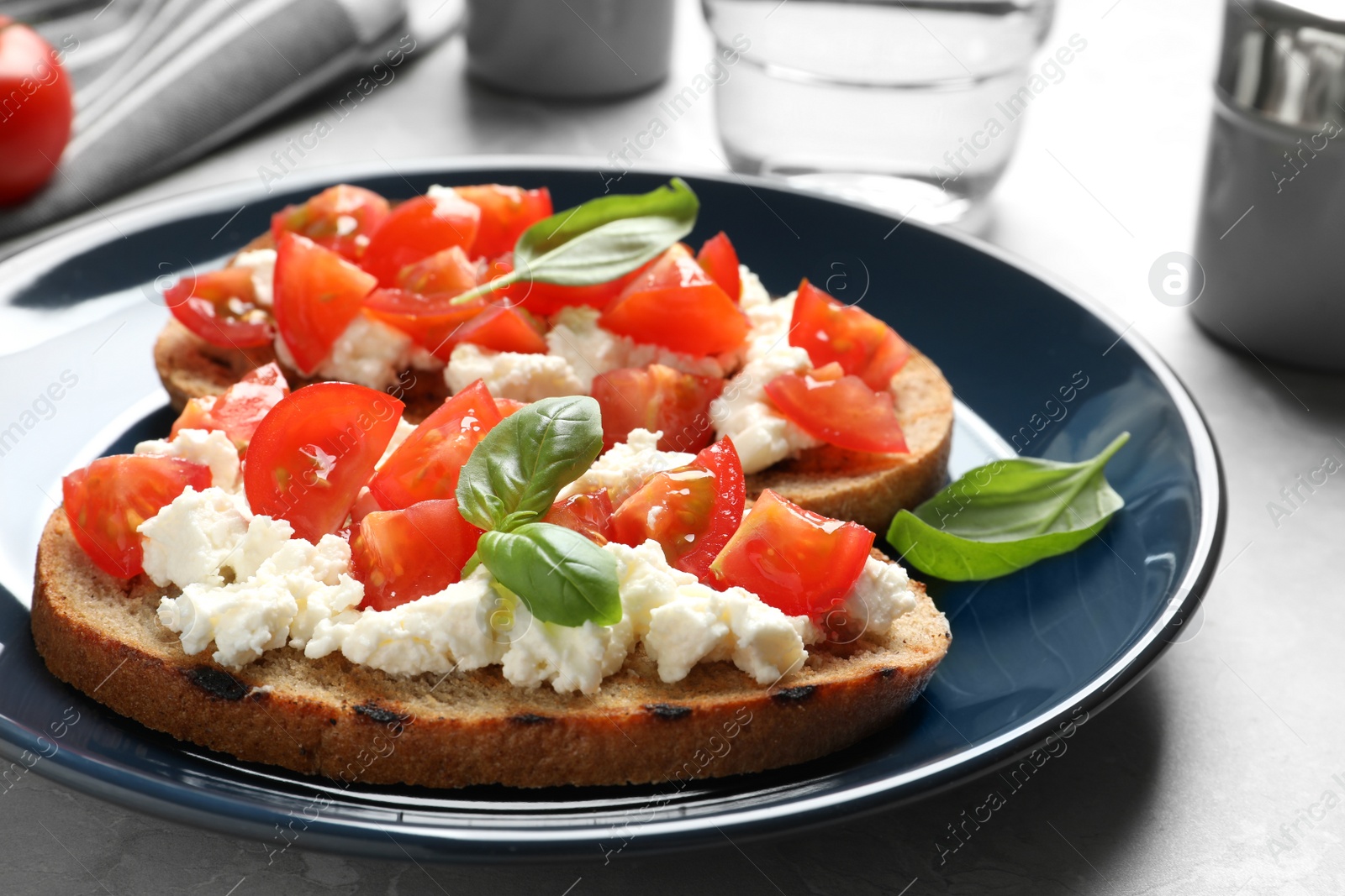 Photo of Plate with tasty bruschettas on grey table, closeup