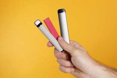 Man holding electronic cigarettes on yellow background, closeup