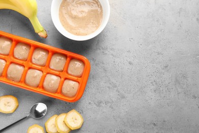Photo of Banana puree in ice cube tray with fresh banana fruits on grey table, flat lay. Space for text
