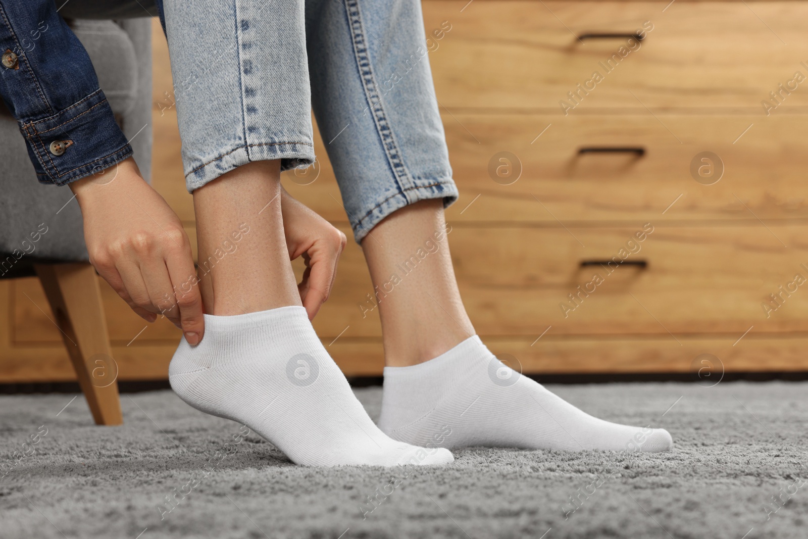 Photo of Woman putting on white socks at home, closeup