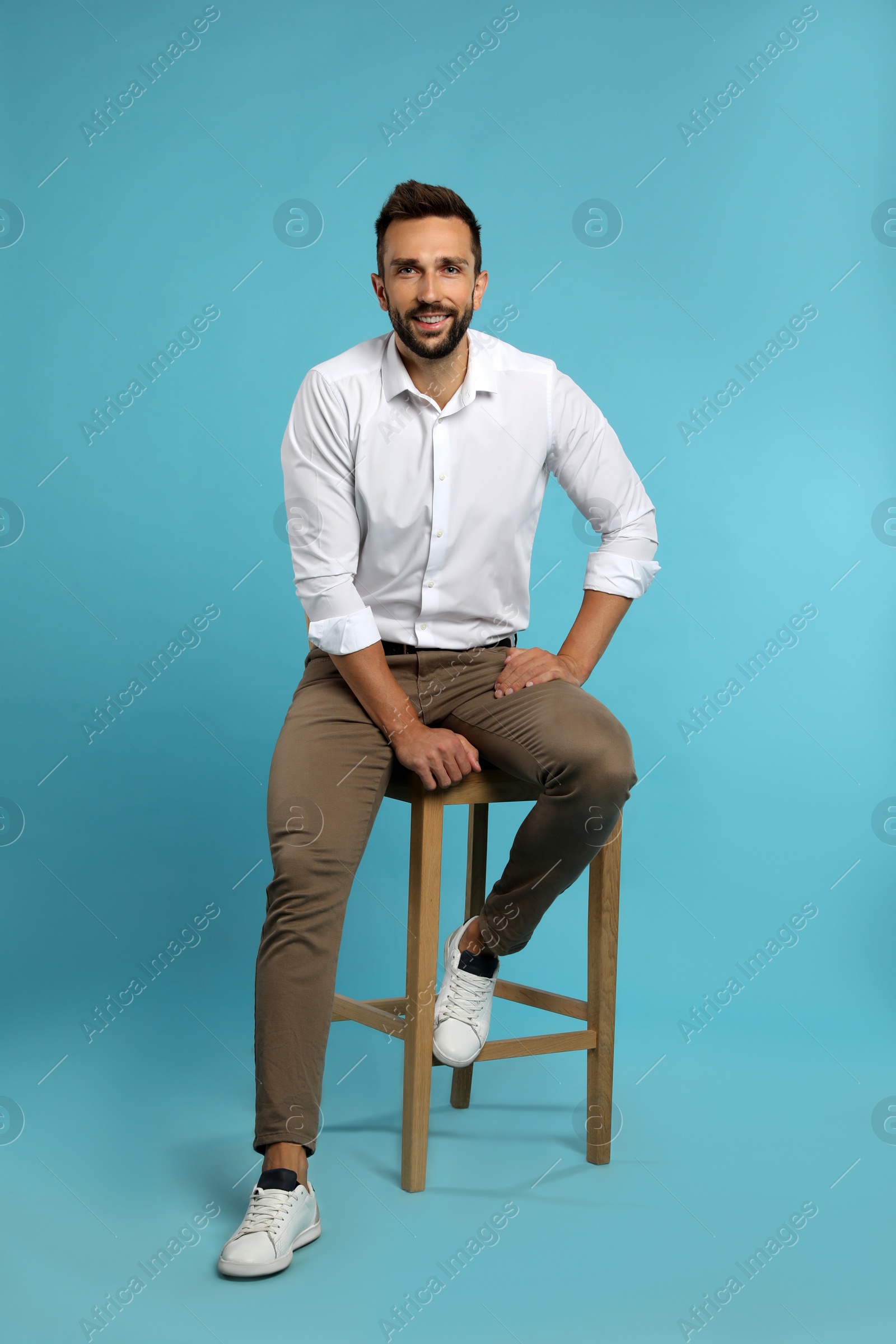 Photo of Handsome man sitting on stool against turquoise background