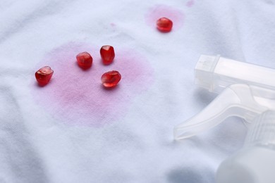 White shirt with fruit juicy stains, detergent and pomegranate seeds as background, closeup