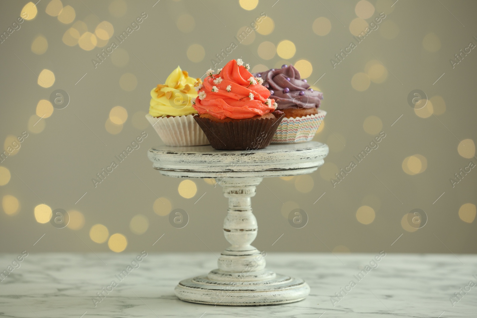 Photo of Different colorful cupcakes on white marble table against blurred lights