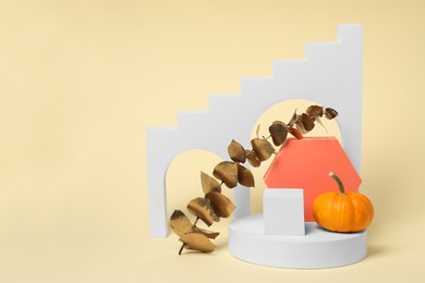 Photo of Autumn presentation for product. Geometric figures, pumpkin and golden branch with leaves on beige background, space for text