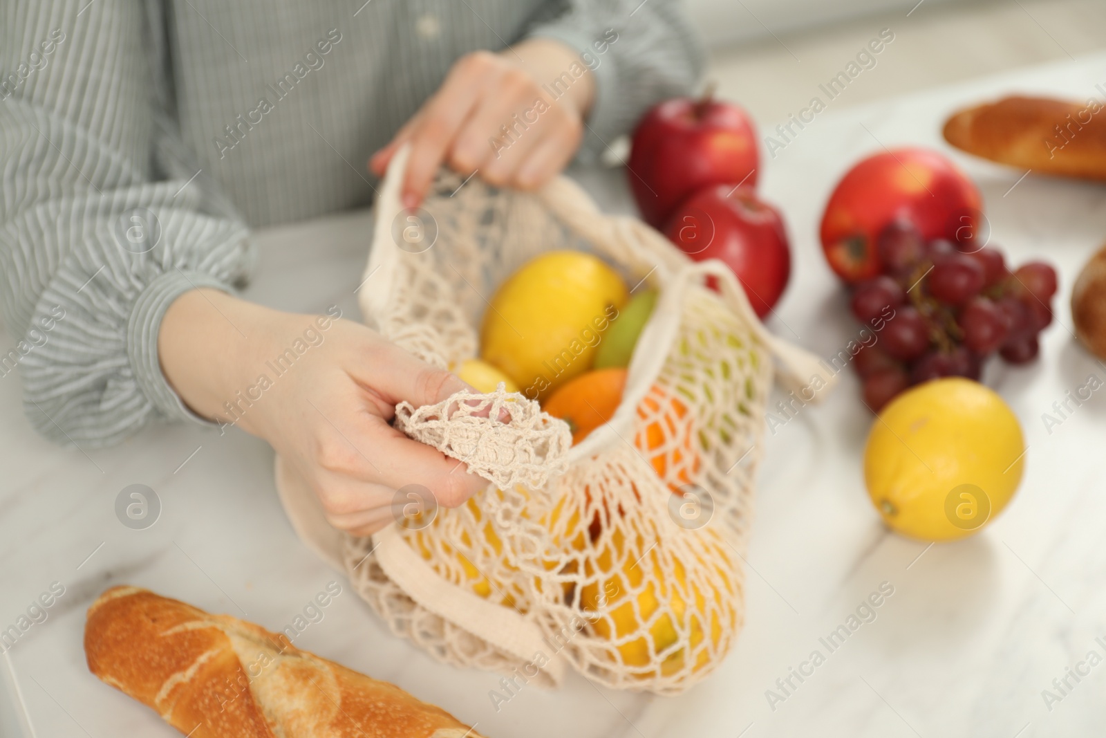 Photo of Woman with string bag of fresh fruits at light marble table, closeup