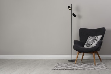 Photo of Armchair with pillow and floor lamp near wall, space for text. Interior design