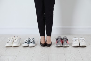 Photo of Different comfortable sneakers near businesswoman wearing high heel shoes indoors, closeup