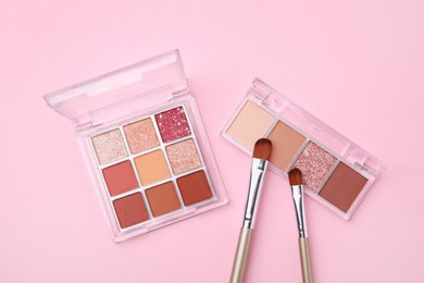 Beautiful eye shadow palettes and brushes on pink background, flat lay