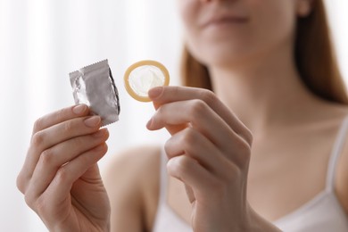 Woman holding unwrapped condom indoors, closeup. Safe sex