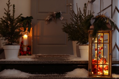 Photo of Decorative lanterns and small Christmas trees near house entrance