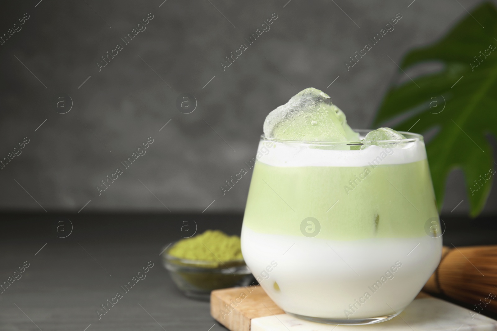 Photo of Glass of tasty iced matcha latte on grey wooden table, closeup. Space for text