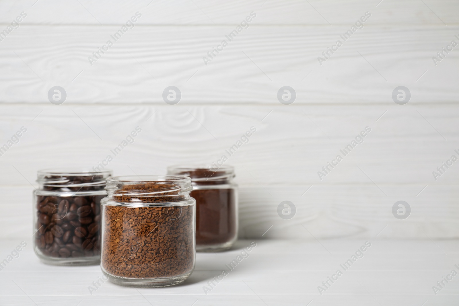 Photo of Jars with instant, ground coffee and roasted beans on white wooden table, space for text