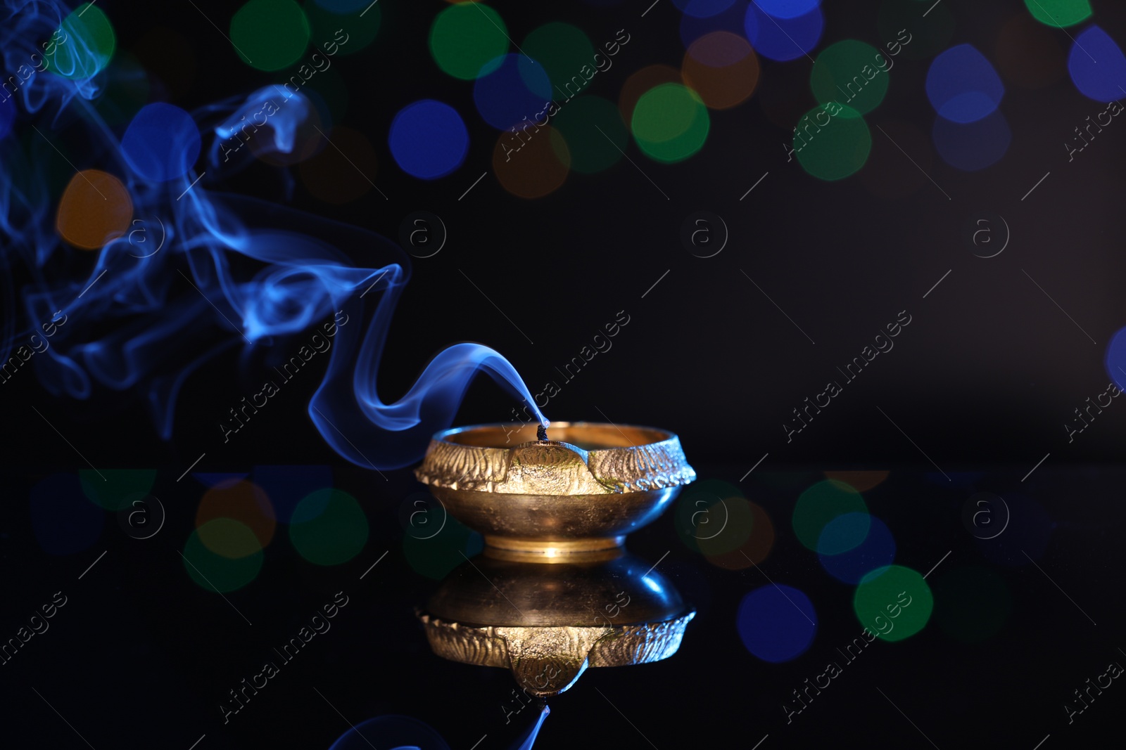 Photo of Blown out diya on dark background with blurred lights, space for text. Diwali lamp