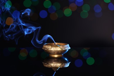 Photo of Blown out diya on dark background with blurred lights, space for text. Diwali lamp