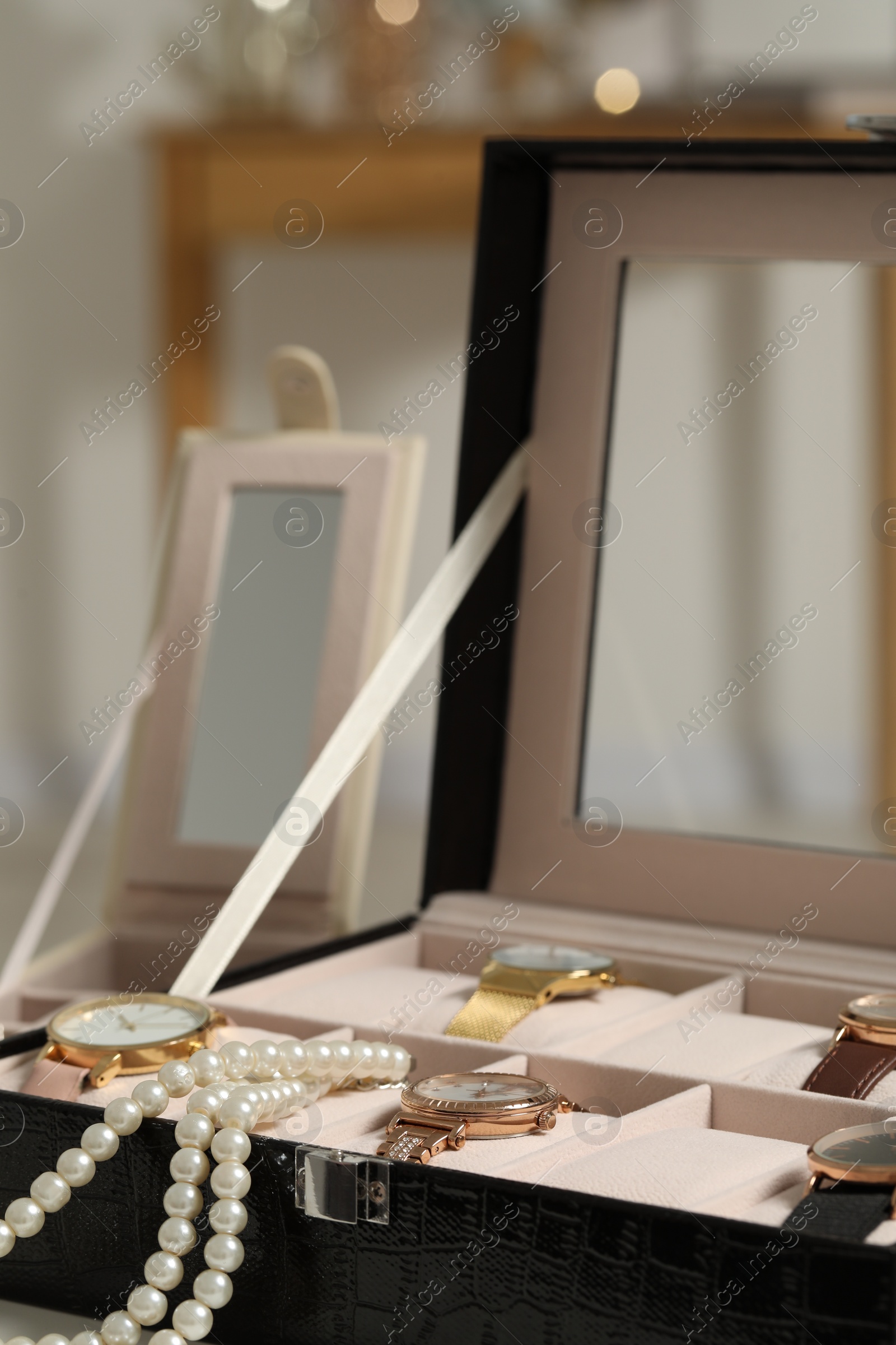Photo of Jewelry box with many stylish wristwatches and pearl necklace indoors, closeup