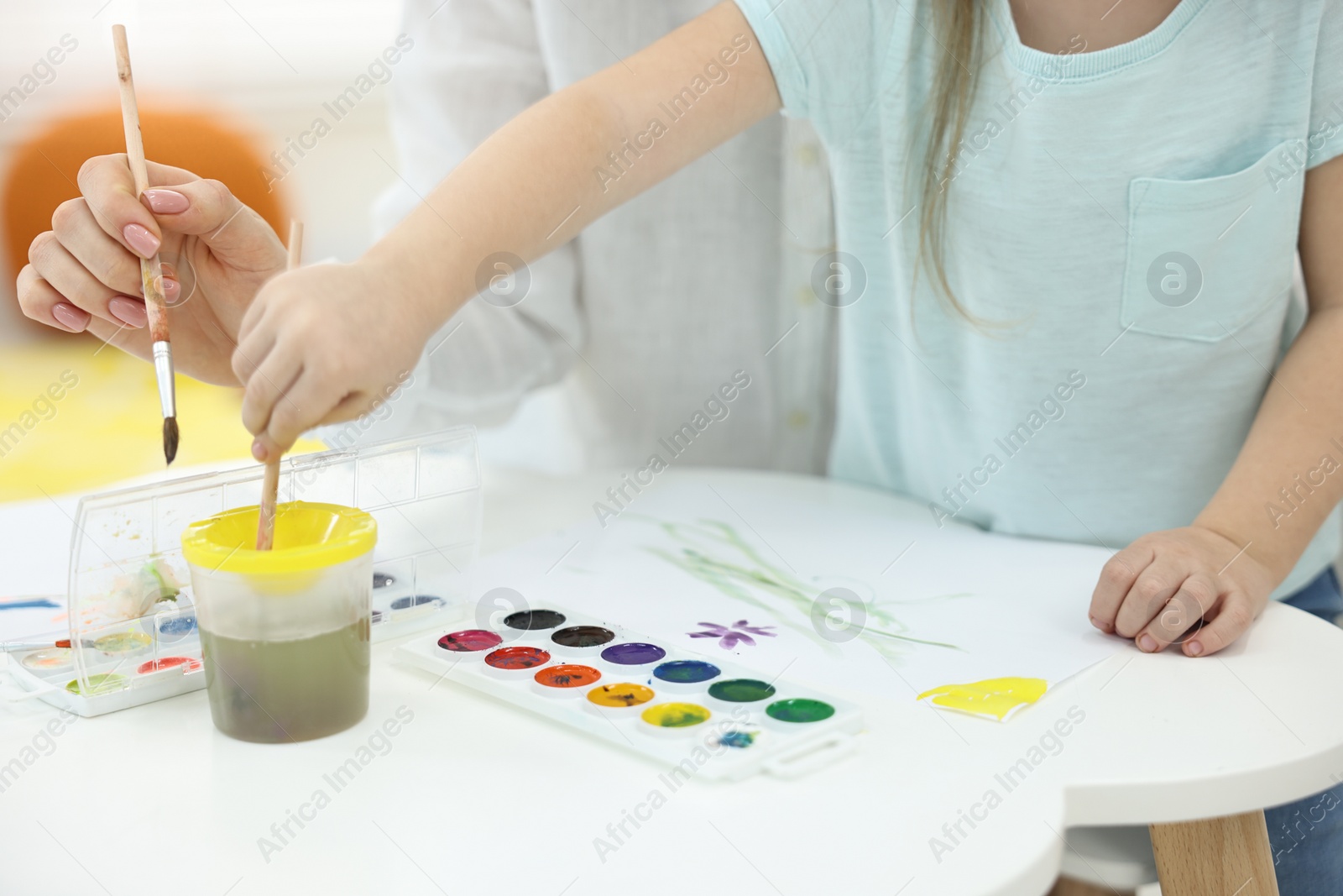 Photo of Mother and her little daughter painting with watercolor at home, closeup